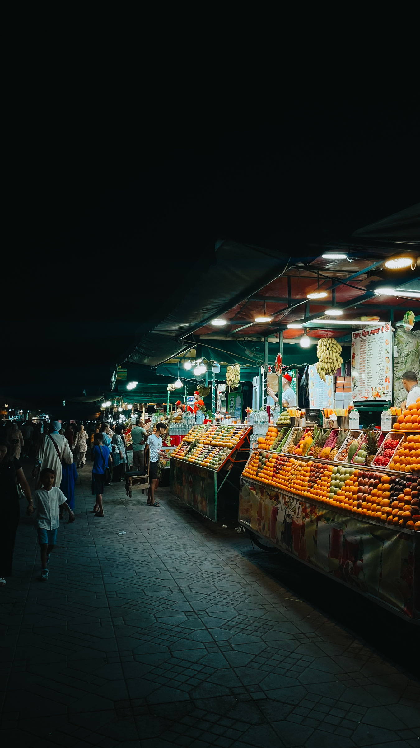 Bancas de fruta iluminadas num mercado à noite
